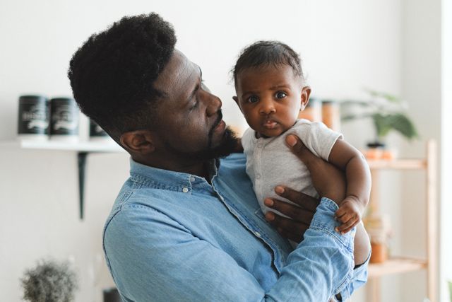 Black father holding his newborn baby at home, reflecting the emotional bond between new dads and their infants
